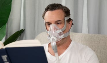 Man reading in bed while wearing an AirFit F20 CPAP mask