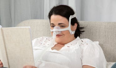 Woman reads a book in bed while wearing AirFit N20 For Her CPAP mask