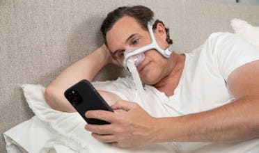 Man wearing AirFit N20 lays in bed, scrolling on his phone