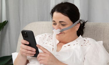 Woman wearing AirFit P10 For Her smiles while looking at phone in bed