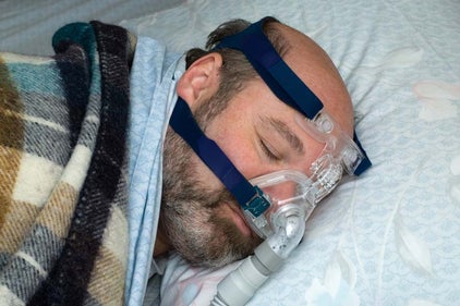 a man with a beard wearing nasal CPAP mask sleeping on his side